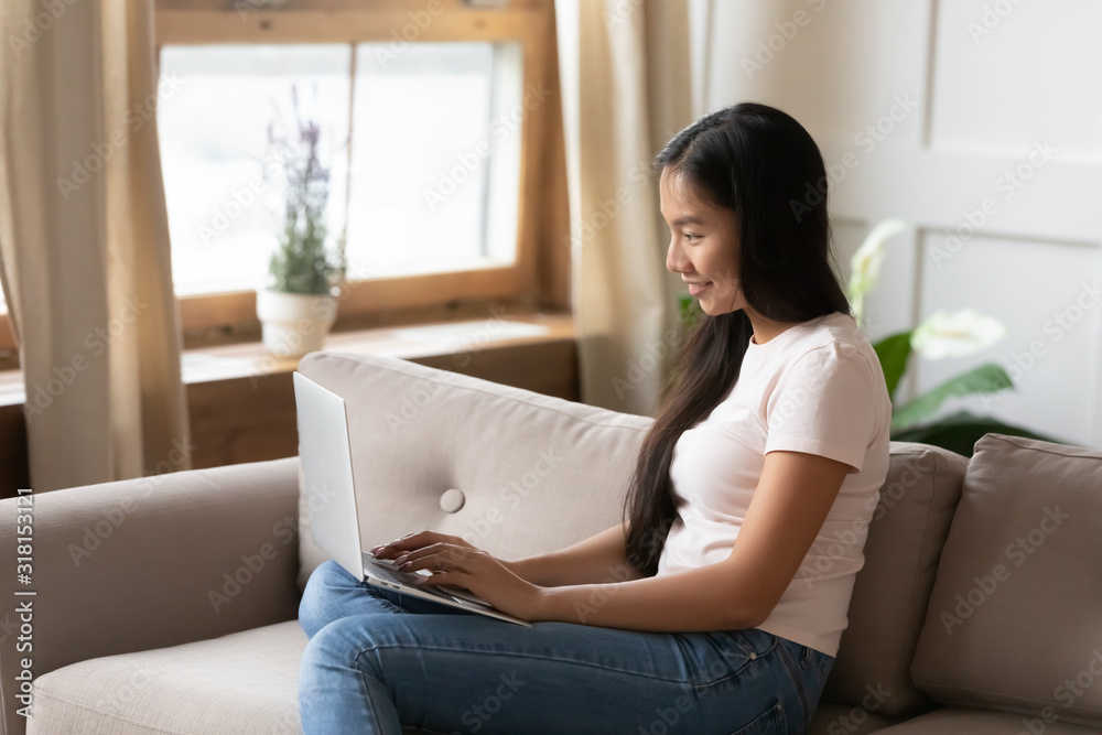 Smiling Vietnamese girl typing on modern laptop at home Smiling Vietnamese girl typing on modern laptop at home