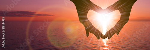 Two hands in the shape of a heart on a sunset background over the sea. The concept of a romantic date, a declaration of love, a love relationship.