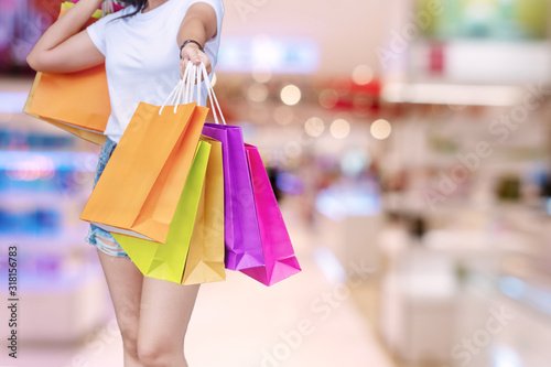 Customer young woman holding shopping bag while standing on blur mall center background. Joyful female carrying shopping paper bag in her hand. Happiness, consumerism, sale and people concept.