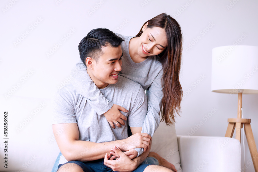 Young woman hugging her boyfriend from back while sitting together on sofa at home. Romantic couple embracing feeling relax in living room. Relationship and valentines day concept. Young woman hugging her boyfriend from back while sitting together on sofa at home. Romantic couple embracing feeling relax in living room. Relationship and valentines day concept.