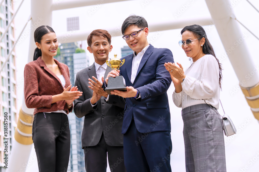 Group of business people clap to congratulate colleagues holding trophy while standing at walkway central business district full tall buildings. They showing excited for team success to win business. Group of business people clap to congratulate colleagues holding trophy while standing at walkway central business district full tall buildings. They showing excited for team success to win business.