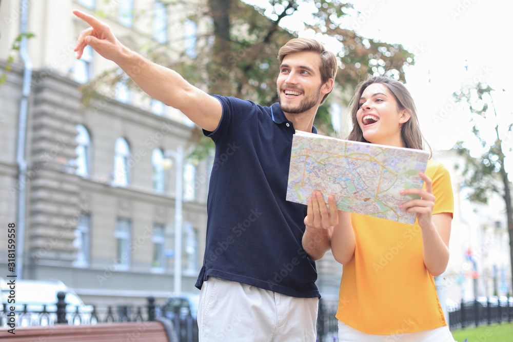 Naklejka premium Beautiful young couple holding a map and smiling while standing outdoors.