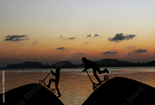 Silhouette boy play spin scooter and bike with the evening atmosphere.