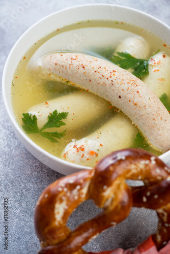 Close-up of boiled weisswurst white sausages served in bouillon with a pretzel, selective focus, vertical shot