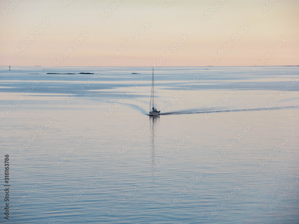 Pastel colored sunset photo with a sailboat at sea and small rocky islands.