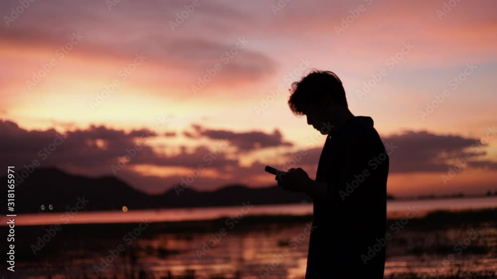 Silhouette of portrait young asian man using smartphone sharing vacation on social media enjoying the view at sea beach beautiful summer sunset, golden hour light. Silhouette of portrait young asian man using smartphone sharing vacation on social media enjoying the view at sea beach beautiful summer sunset, golden hour light.