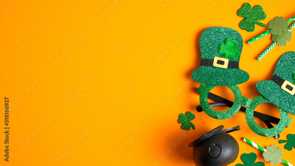 Happy St Patrick's Day concept. Flat lay composition with St Patricks Day party glasses, drinking straws decorated shamrock leaf clovers, pot of gold on orange background. Greeting card, banner design Happy St Patrick's Day concept. Flat lay composition with St Patricks Day party glasses, drinking straws decorated shamrock leaf clovers, pot of gold on orange background. Greeting card, banner design