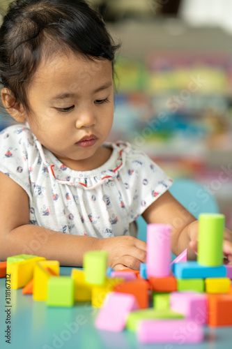 Cute little girl playing with multicolor wooden building blocks on blue table.