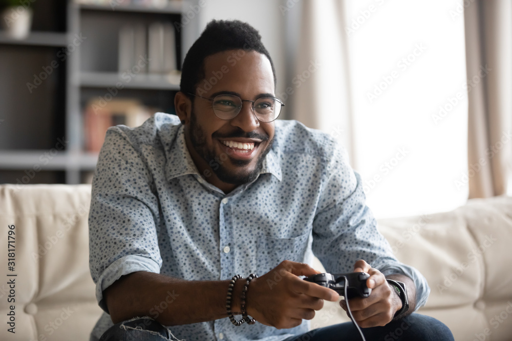 Happy young african guy holding joystick controller playing video game - obrazy, fototapety, plakaty 
