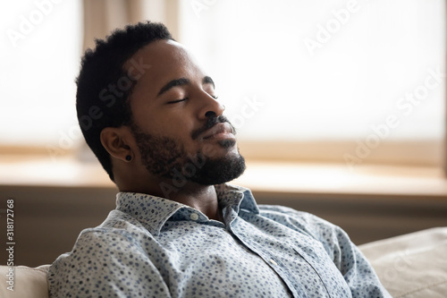Tranquil young african man resting eyes closed breathing on couch photo