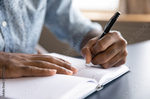Close up view of african left-handed businessman writing in notebook photo