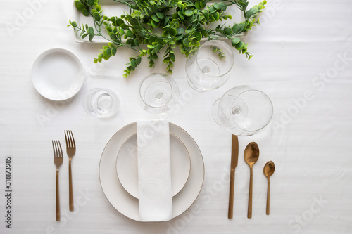 Elegant table setting, white plates, gold cutlery, wine glasses and centrepiece . Tableware and decorations for serving a festive table