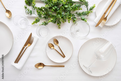 Tableware background in white gold tone.White plates,  gold cutlery,  wine glasses and decorative plant centrepiece