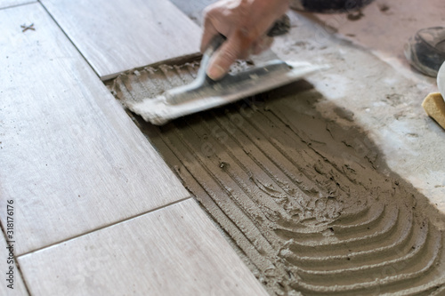 Man installing rectangular shaped floor tiles in kitchen. Applying adhesive before installation and verifying afterwards