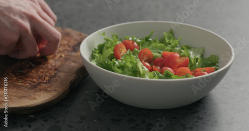 man hands preparing salad with mozzarella, cherry tomatoes and frisee leaves in white bowl on terrazzo surface