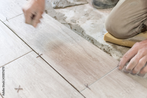 Man installing rectangular shaped floor tiles in kitchen. Applying adhesive before installation and verifying afterwards