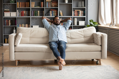 Serene barefoot african man resting on sofa hands behind head photo