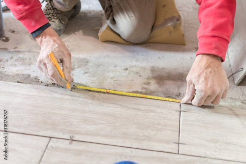 Man installing rectangular shaped floor tiles in kitchen. Applying adhesive before installation and verifying afterwards