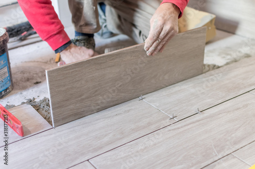 Man installing rectangular shaped floor tiles in kitchen. Applying adhesive before installation and verifying afterwards