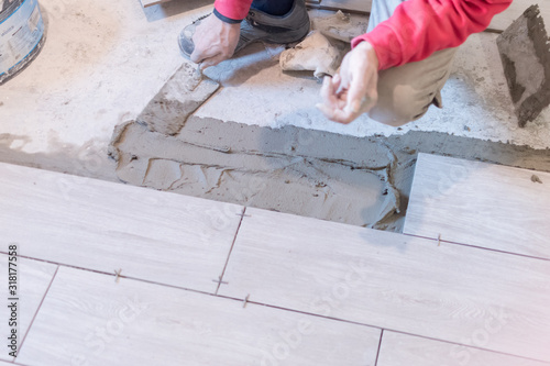 Man installing rectangular shaped floor tiles in kitchen. Applying adhesive before installation and verifying afterwards