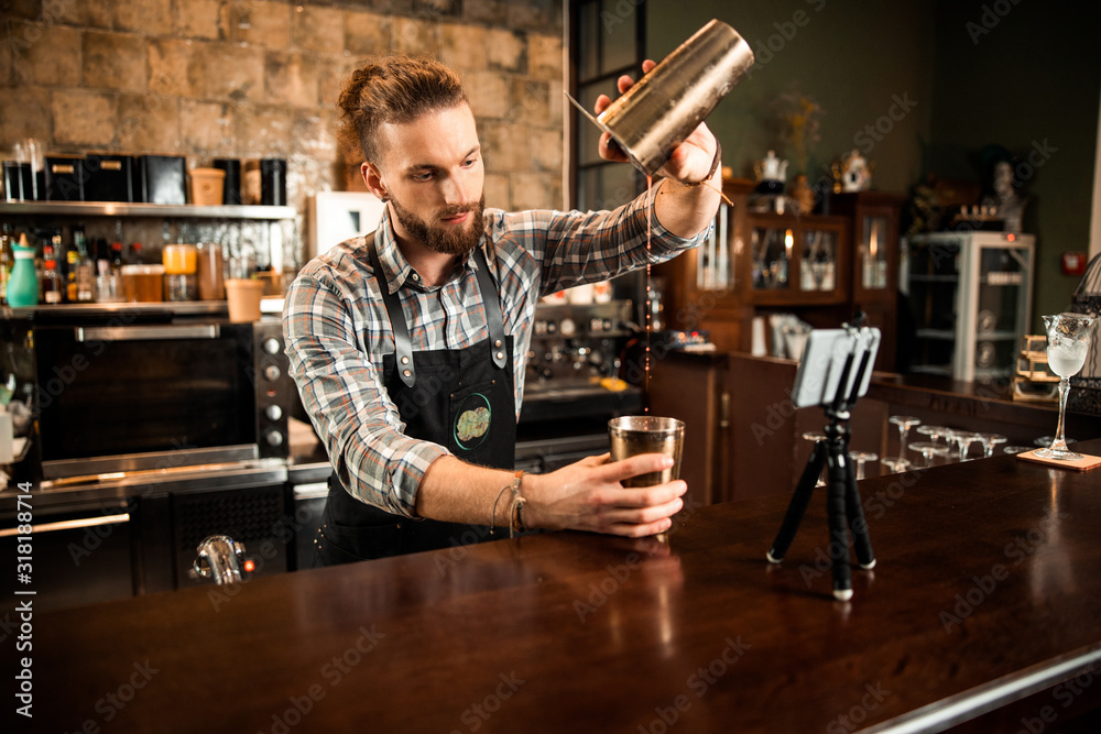 Fotografie Bearded barman pouring drink from shaker