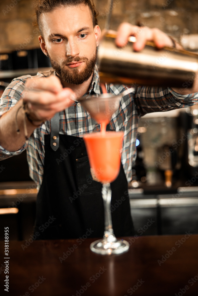 Bearded barman is pouring cocktail into the glass