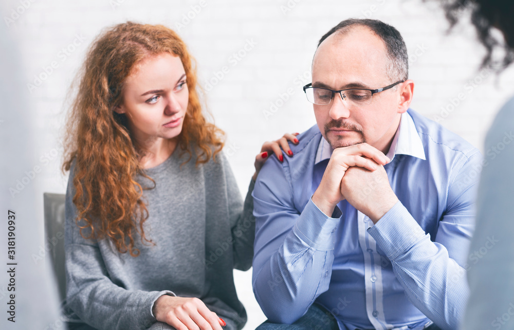 Supportive wife comforting her upset husband at meeting in counselor's office Supportive wife comforting her upset husband at meeting in counselor's office