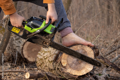 Logging with chainsaw with no equipment. Dangers of logging. Green chainsaw and bare foot cutting the wood in forest.