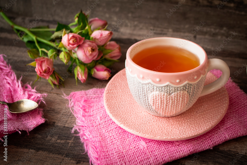 Close up of a cup of tea with roses and chocolate candies on wooden table Close up of a cup of tea with roses and chocolate candies on wooden table