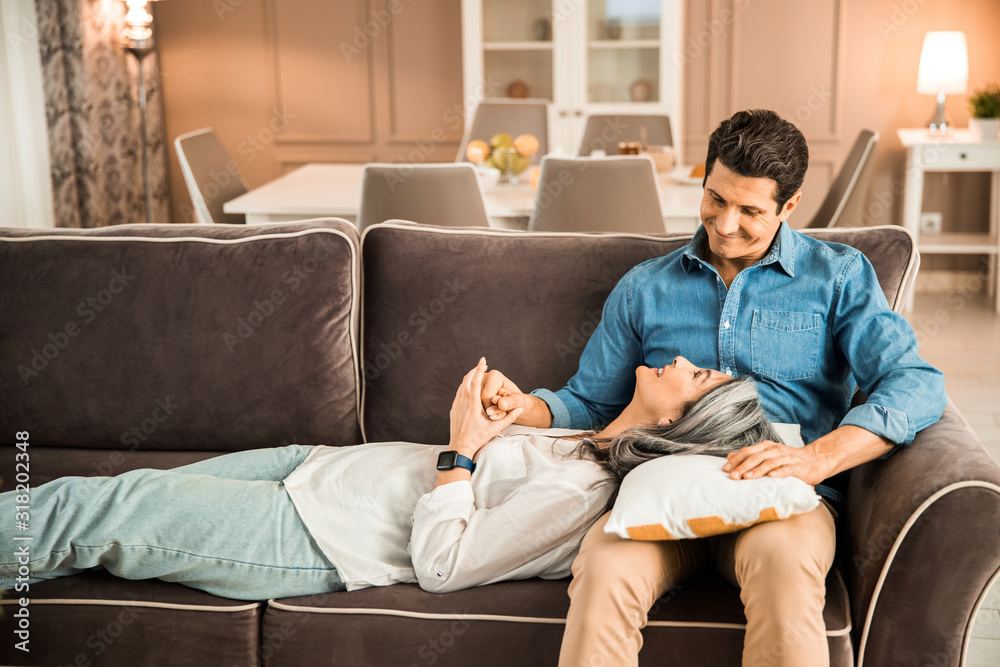 Happy adult woman lying on sofa and looking at man at home