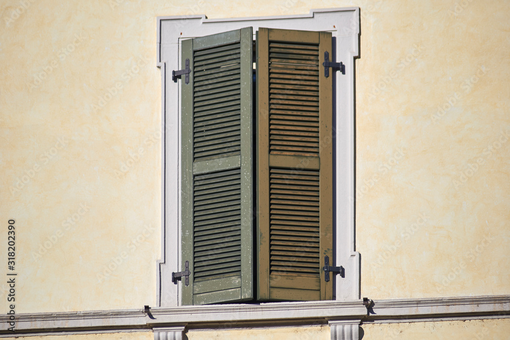 Italian window on the bright wall facade with closed wooden green shutters