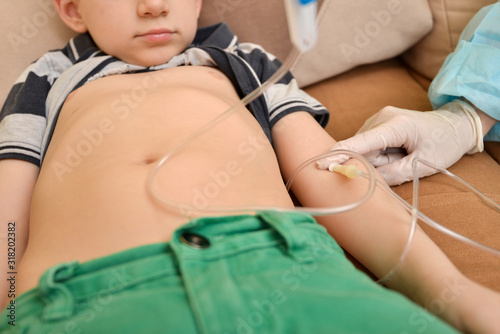 The doctor gives an injection to an ill child with an intravenous dropper at home.