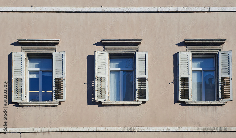 Three italian windows on the beige color wall facade with open wooden shabby white shutters