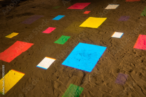 Square shapes of different sizes and colors on the sand.