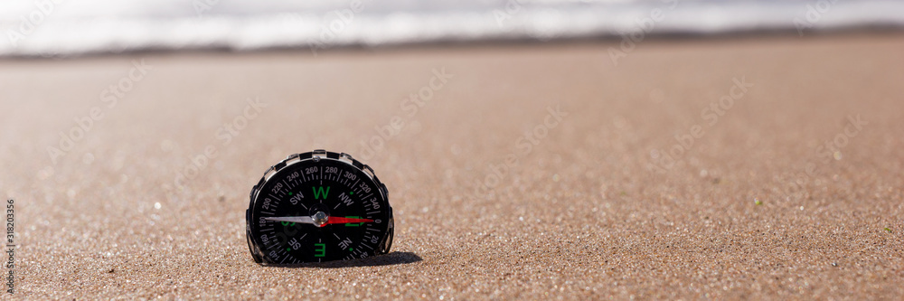 Compass in the sea sand at the beach, water in background. Panoramic image Compass in the sea sand at the beach, water in background. Panoramic image
