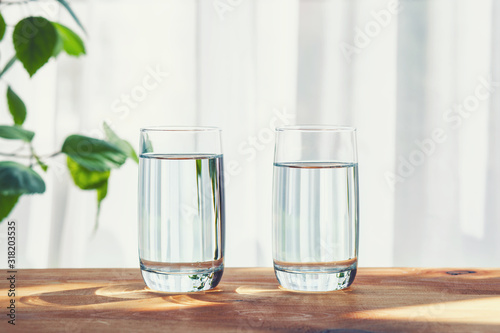 two glasses of water standing on wooden table inside, copy space