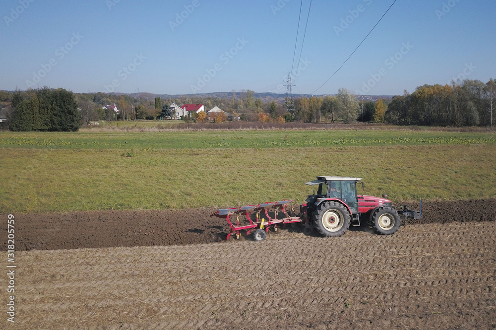 Obraz premium A farmer on a red tractor with a seeder sows grain in plowed land in a private field in the village area. Mechanization of spring field work. Farmer's everyday life. Processing of land. The agrarian
