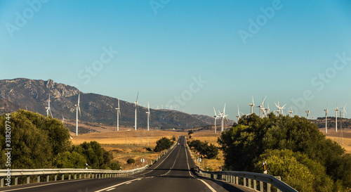 Large group of white wind generators produces alternative energy by wind on the fields in Europe in Spain on the both side of a road with cars