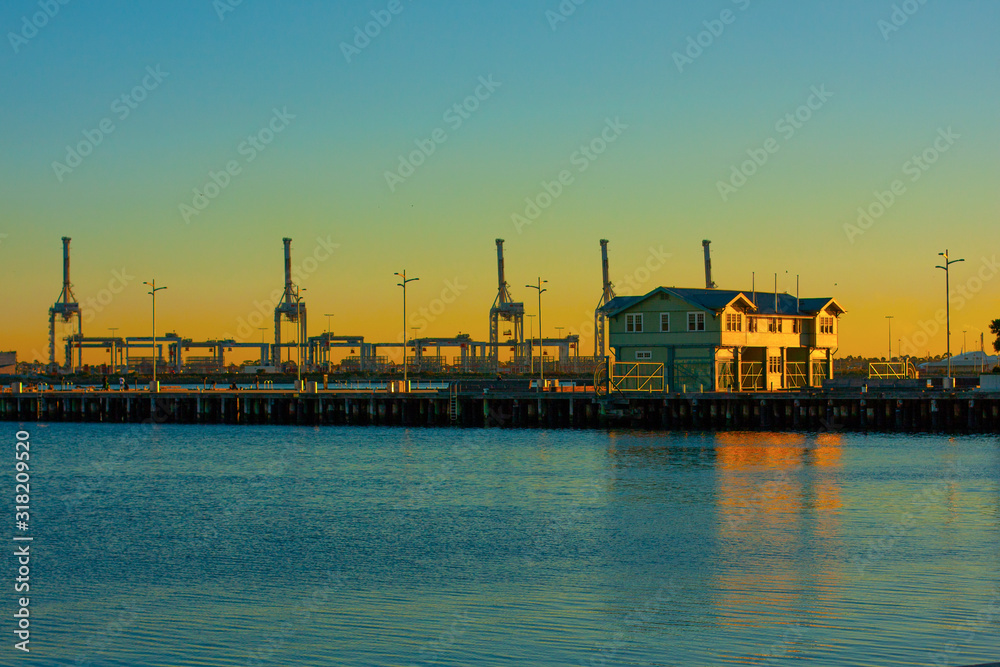 A pier in the port and port loading cranes in the distance against the beautiful sunset sky.