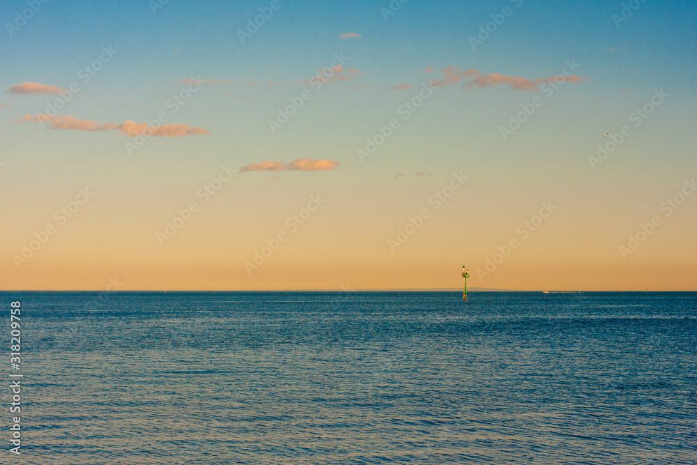 A beautiful calm ocean without waves with a slight rippling of several white clouds in the sky. Port of Melbourne, Australia.