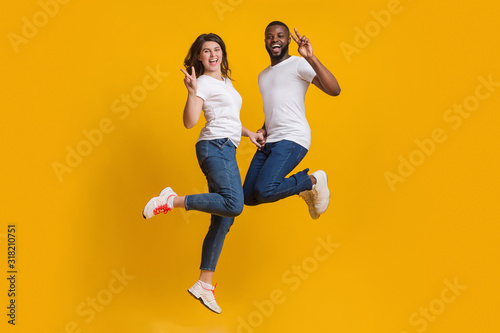 Happy Couple Fooling Together, Jumping In Air And Showing Peace Sign