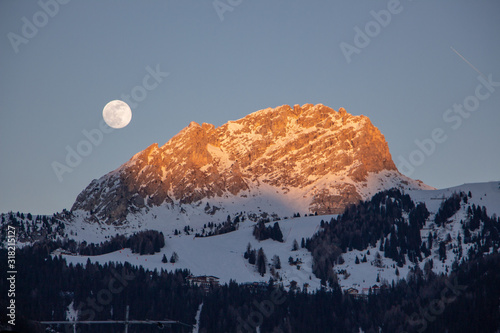 Moon rise and sunset over Italy dolomites with gorgeous light and snowy mountains val di fassa