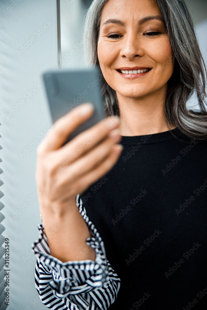 Mirthful smartphone user standing and smiling stock photo Mirthful smartphone user standing and smiling stock photo