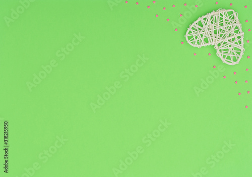 Valentine's Day green background with white rattan and small pink hearts. Greeting or invitation card. Wedding, love, happiness concept. Flat lay, top view with copy space.