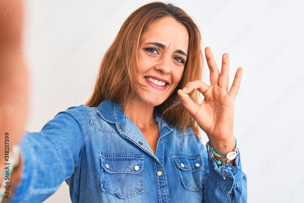 Young redhead woman taking a selfie over isolated background doing ok sign with fingers, excellent symbol Young redhead woman taking a selfie over isolated background doing ok sign with fingers, excellent symbol
