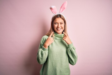 Young beautiful woman wearing easter rabbit ears standing over isolated pink background smiling cheerful showing and pointing with fingers teeth and mouth. Dental health concept.