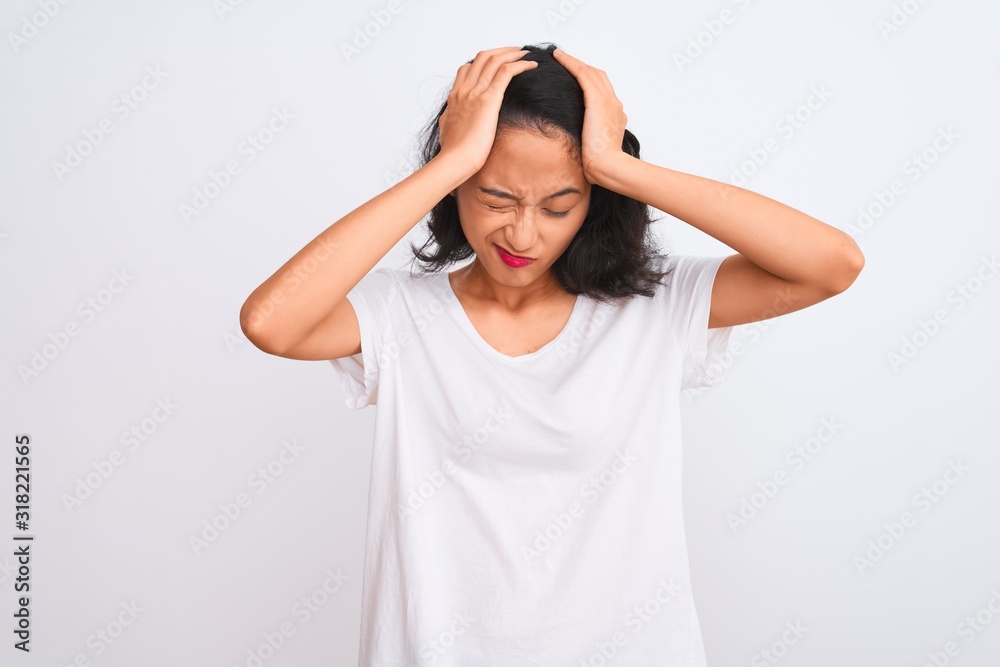 Young chinese woman wearing casual t-shirt standing over isolated white background suffering from headache desperate and stressed because pain and migraine. Hands on head. Young chinese woman wearing casual t-shirt standing over isolated white background suffering from headache desperate and stressed because pain and migraine. Hands on head.