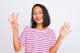Young chinese woman wearing striped t-shirt standing over isolated white background showing and pointing up with fingers number nine while smiling confident and happy.