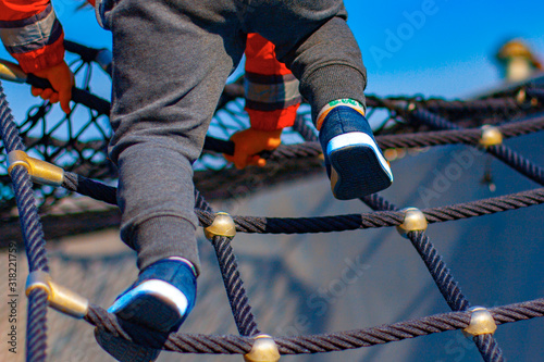 A boy on the playground climbing on a rope-ladder (web). A view of legs and arms on the sky background