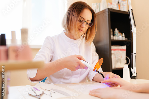 Medicine  nail Polish and prosthetic nail. A manicure master performs a procedure for prosthetics of the nail using an ultraviolet lamp